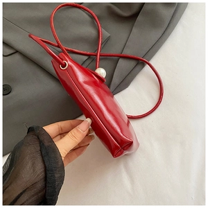 Detail of red mini leather phone bag featuring a large pearl embellishment and thin strap