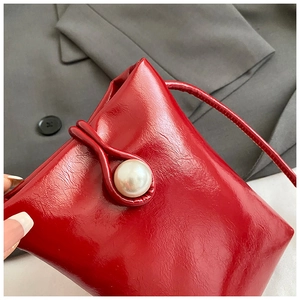 Detail of red crossbody phone bag featuring a large pearl clasp and glossy finish
