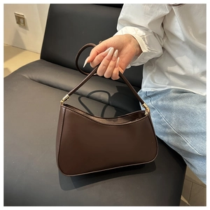 Détail du sac croissant marron foncé avec ferrures dorées sur un fauteuil en cuir noir