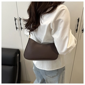 Detailed side view of a minimalist deep brown leather underarm bag worn by a model