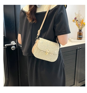 Detailed view of floral embroidery and gold horseshoe buckle on the straw saddle bag