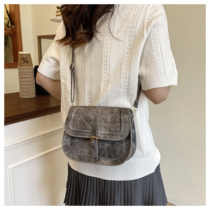 Retro grey saddle bag shown in a cozy cafe setting with detailed leather texture