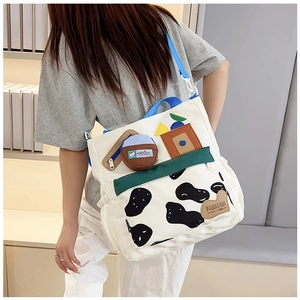 Detail of canvas tote bag with blue strap, cow print pocket and fashion brand tag
