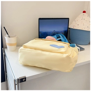 Detail of light yellow nylon tote bag featuring blue heart patch and adjustable strap