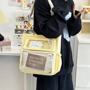 Pale yellow canvas shoulder bag with clear display pocket and dual handles in daily setting