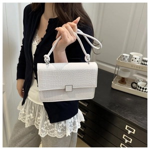 Close-up of white crocodile pattern shoulder bag with metallic buckle and knot handle detail