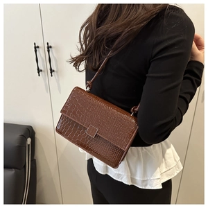 Detail of dark brown faux crocodile leather flap bag with square metal clasp and strap
