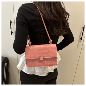 Detailed view of pink croc-embossed small square bag with silver lock worn by model