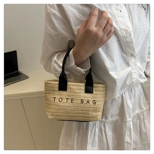 Detail of woven straw tote bag with black PU handles and embroidered lettering