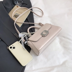 Detailed shot of beige crossbody bag with silver G-buckle, pearl chain, and lace ribbon