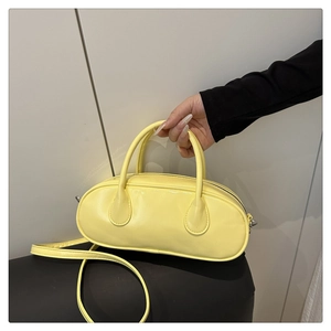 Hand holding pale yellow oval baguette bag with glossy finish and thin shoulder strap