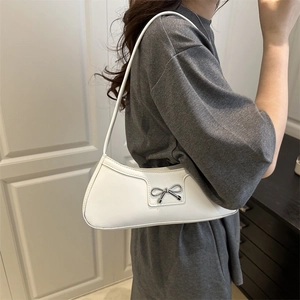 White faux leather baguette shoulder bag with silver bow accent on a female model
