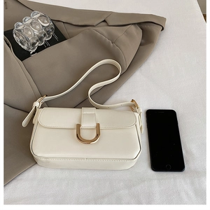 Detail view of cream leather baguette bag with gold horseshoe buckle and smartphone for scale