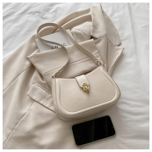 Detail view of cream leather half-moon bag with gold buckle on beige blazer