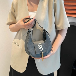 Sac croissant rétro gris avec pompon doré et détails argentés porté par un modèle