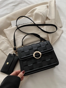 Close-up of black quilted crossbody bag with pearl gold buckle and small hanging pouch
