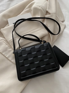 Detail view of mini black crossbody bag with embossed grid pattern and gold hardware