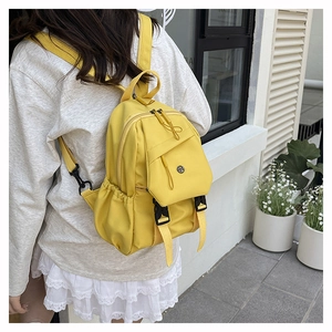 Side view of a bright yellow nylon backpack worn by a model against a white wall