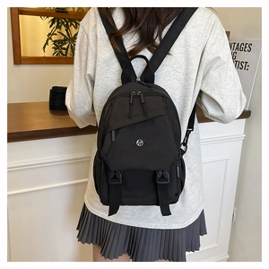 Detail view of a black nylon backpack with a fashion side tag and front buckle straps