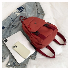 Detail view of burgundy nylon backpack with fashion label and buckle on white fabric