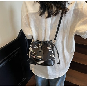 Detail of black drawstring bucket bag featuring colorful wave embroidery and leather strap