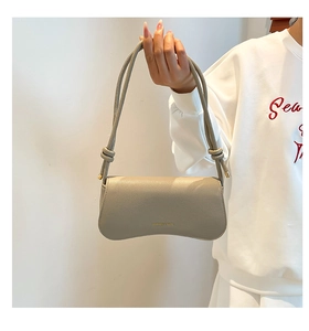 Close-up of beige lychee texture leather bag with unique curved base and knotted strap