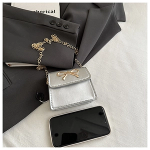 Close-up of mini silver chain bag with gold bow buckle placed next to a smartphone