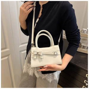 Detail of white square crossbody bag with bow design and silver metal buckle on model