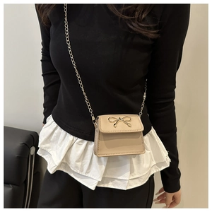 Dettaglio mini borsa a sella beige con fiocco dorato e catena indossata dalla modella