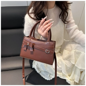 Detail shot of brown vintage handbag with bow and strap accents on a model