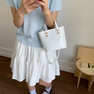 Chic white bucket handbag with gold rivets and leather shoulder strap in a cozy setting