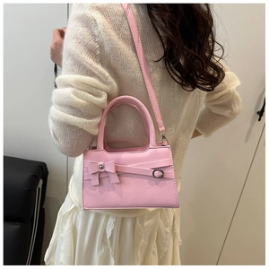 Detail of soft pink crossbody bag with decorative bow, styled on a textured white sweater