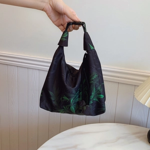 Hobo tote bag with green leaf print and plastic buckle handle against a white background