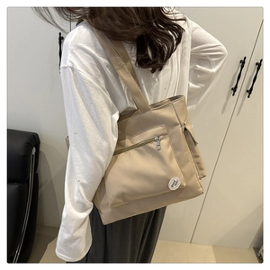 Detail of khaki tote bag showing front zipper pocket and decorative good luck label