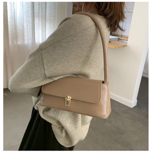 Gros plan du sac baguette en cuir kaki avec boucle dorée sur un mannequin en lumière chaude