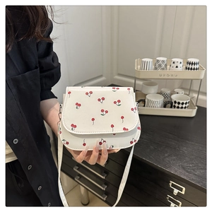 Detail of white saddle bag with red cherry print and slender leather shoulder strap