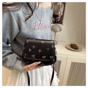 Detail of black faux leather saddle bag featuring red cherry prints and adjustable strap
