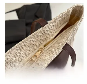 Close-up of golden metal zipper and brown leather trim on a woven straw tote bag