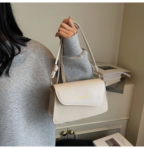 Detail of cream white textured shoulder bag featuring gold FASHION & BAGS logo and strap