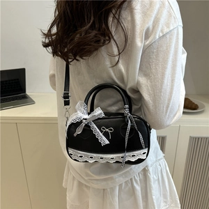 Schwarze Boston-Tasche mit Spitze, Schleifen-Detail und Riemen, getragen in gemütlichem Ambiente