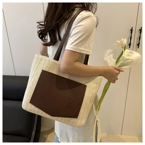 Detail of woven straw tote bag with brown leather bear patch and shoulder strap
