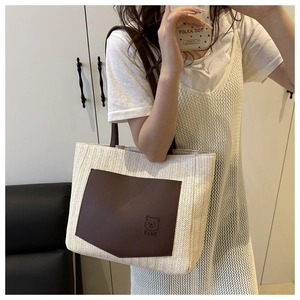 Detail of straw tote bag featuring a leather pocket with a bear print and dark handles