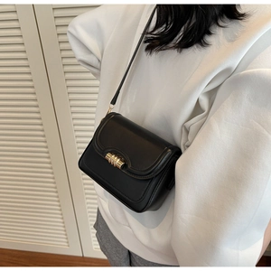 Detail of black PU leather crossbody bag with cylindrical gold metal clasp on a white hoodie
