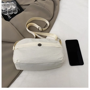 Close-up of beige nylon crossbody bag with adjustable strap and metallic round detail