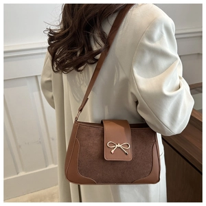 Detail of a brown leather shoulder bag with a small gold bow-knot buckle and suede panel