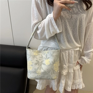 Floral embroidered bucket bag in sage green shown with a soft fashion outfit for summer