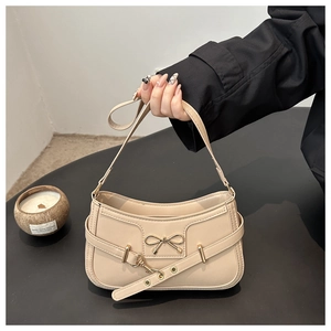 Detalle de bolso de hombro beige con lazo metálico y correa con ojales decorativos