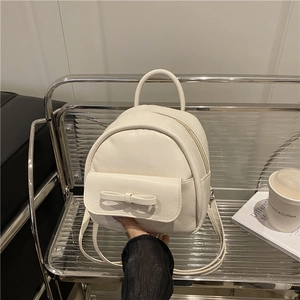 Mini cream PU leather backpack with bow accent on a stylish modern chair