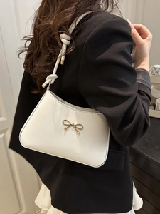 Detail of white half-moon bag featuring a gold bow buckle and woven rope shoulder strap