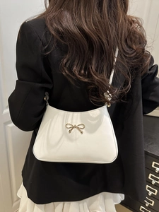 Detailed back view of a white shoulder bag with a gold bow accent on model in home setting